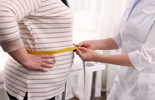 overweight woman having waist measured by a doctor